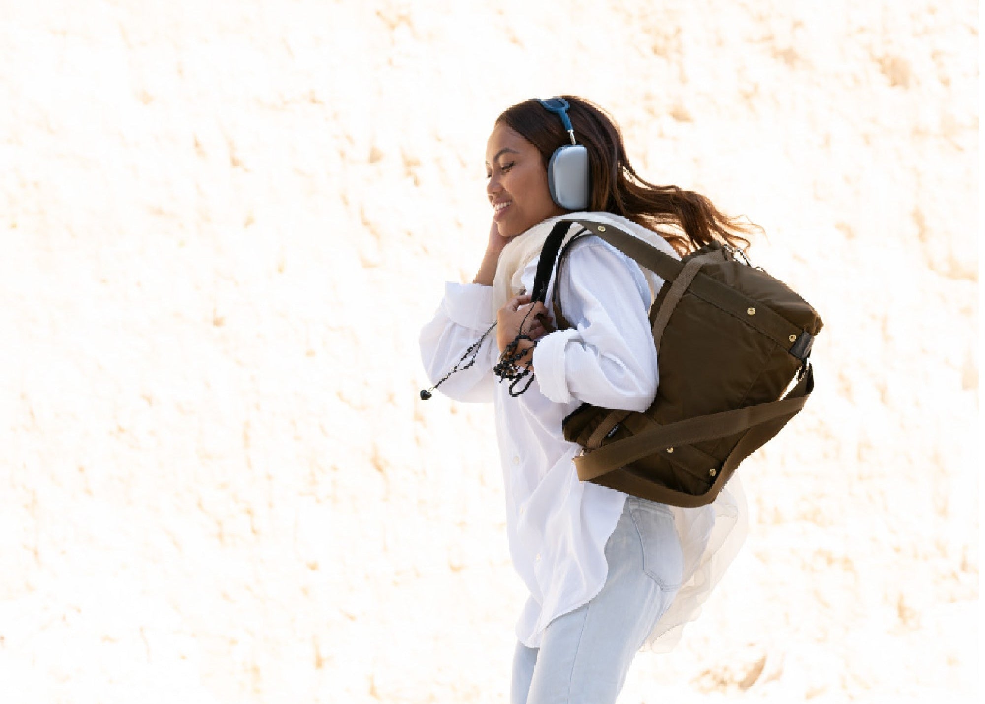 Person wearing a white jacket and light blue jeans with a brown backpack on a white background